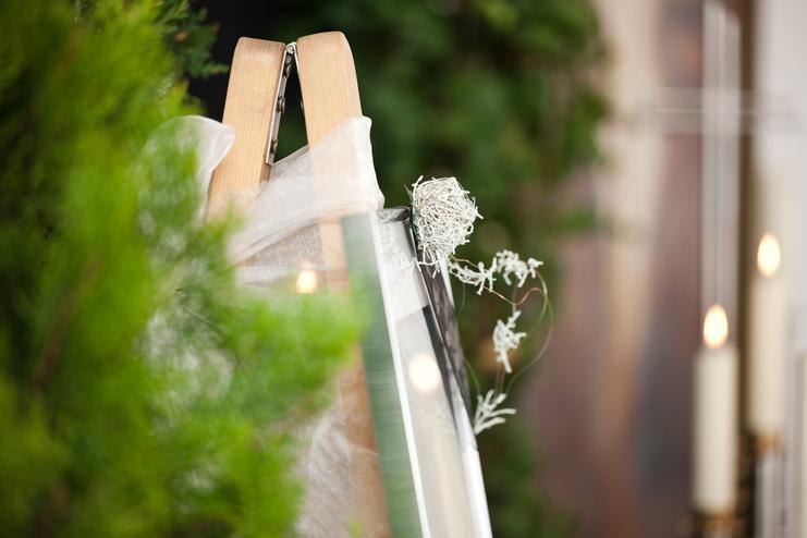 Staffelei mit einem eingewickelten Bilderrahmen und dekorativen Zweigen vor unscharfem, grünem Hintergrund.